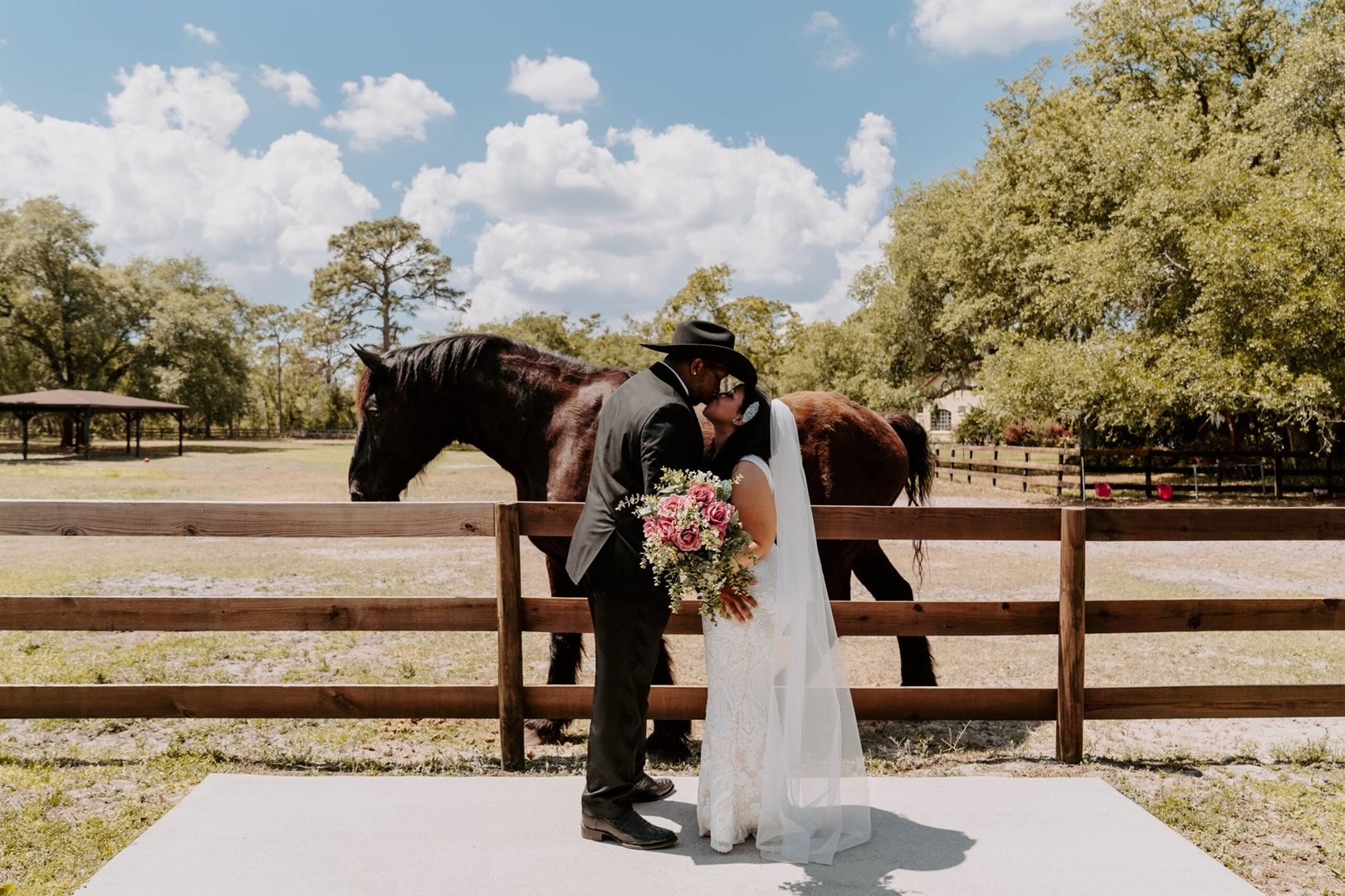 A couple kissing in front of a wooden fence and magical brown horse at BLB Hacienda