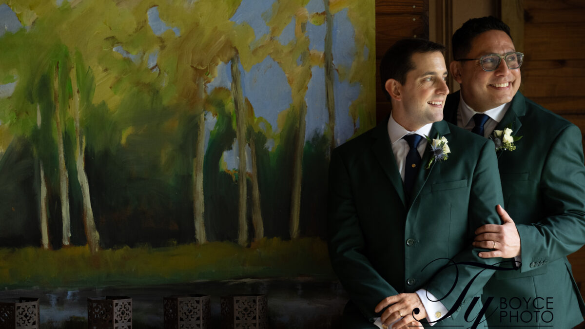 Two grooms gazing at each other in front of a forest landscape artwork