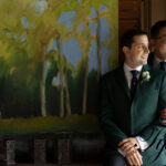 Two grooms gazing at each other in front of a forest landscape artwork