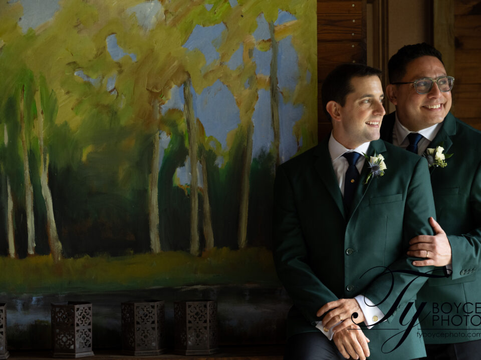 Two grooms gazing at each other in front of a forest landscape artwork