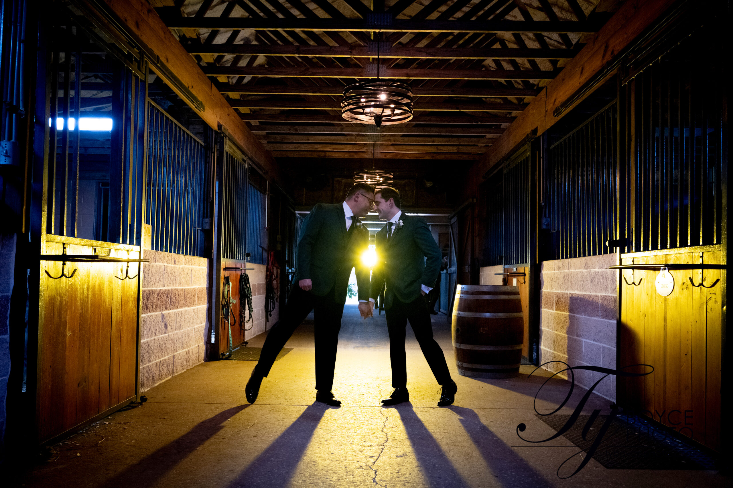 Two grooms in the golden hour leaning towards each other in the barn