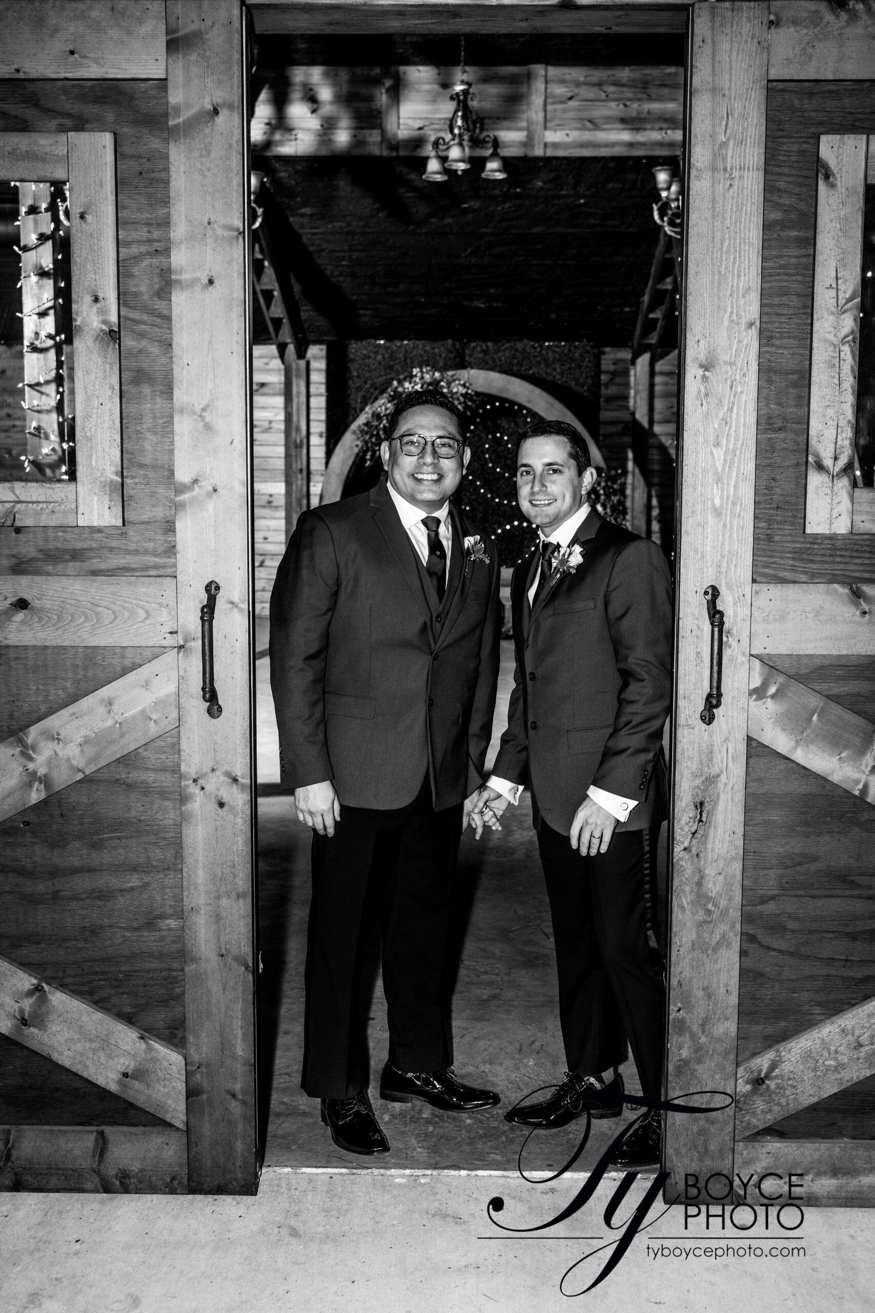 Two grooms standing in the picturesque barn doors of BLB Hacienda