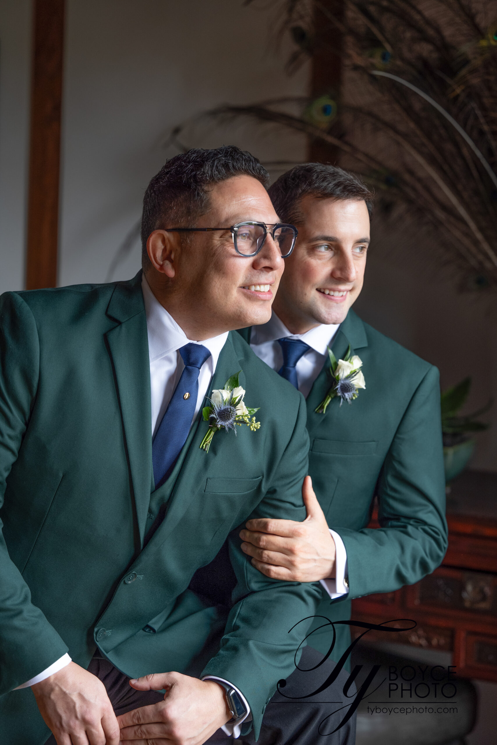 Two grooms in green blazers gazing outward on their wedding day