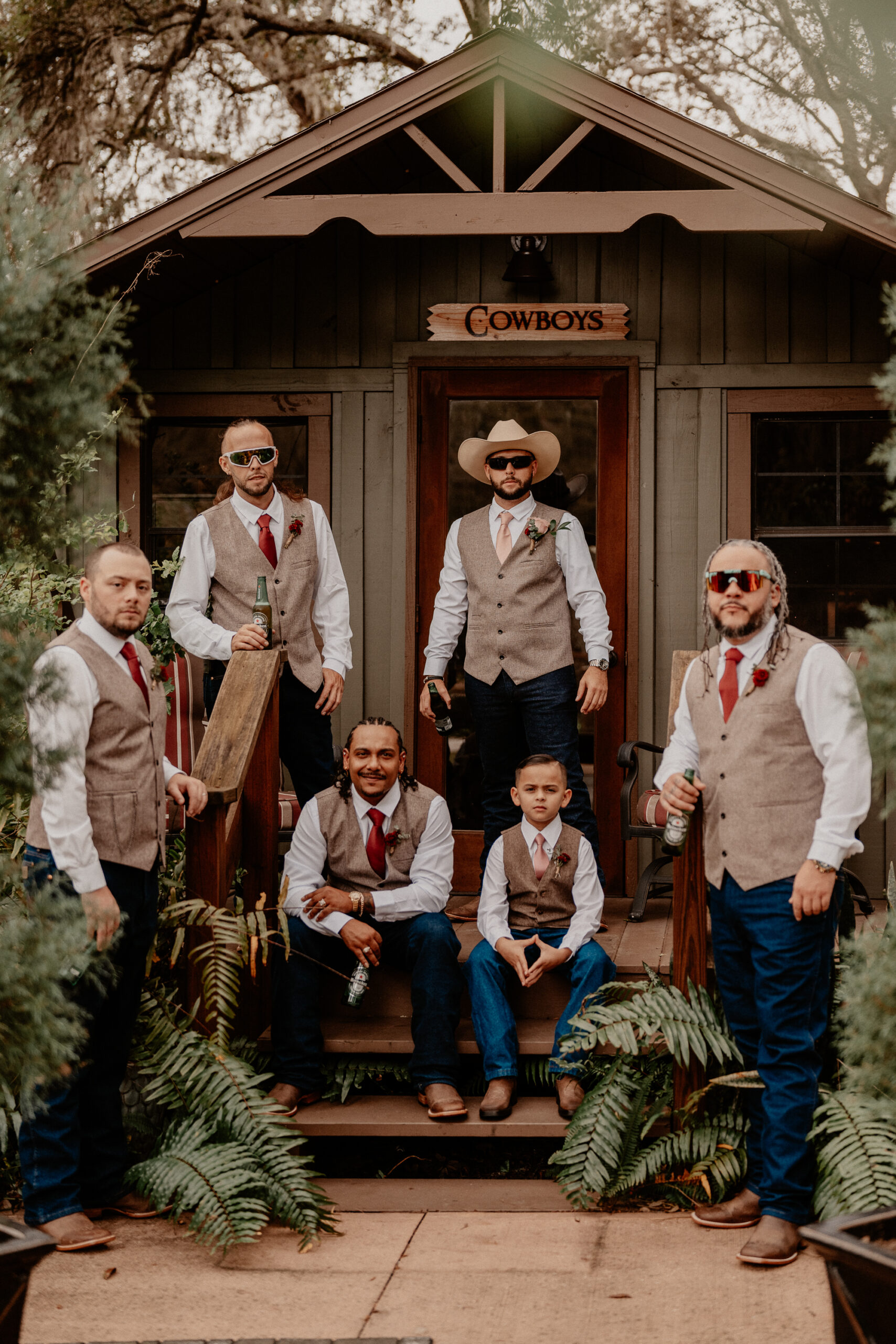 The groomsmen standing in front of the rustic grooms cabin labeled cowboys