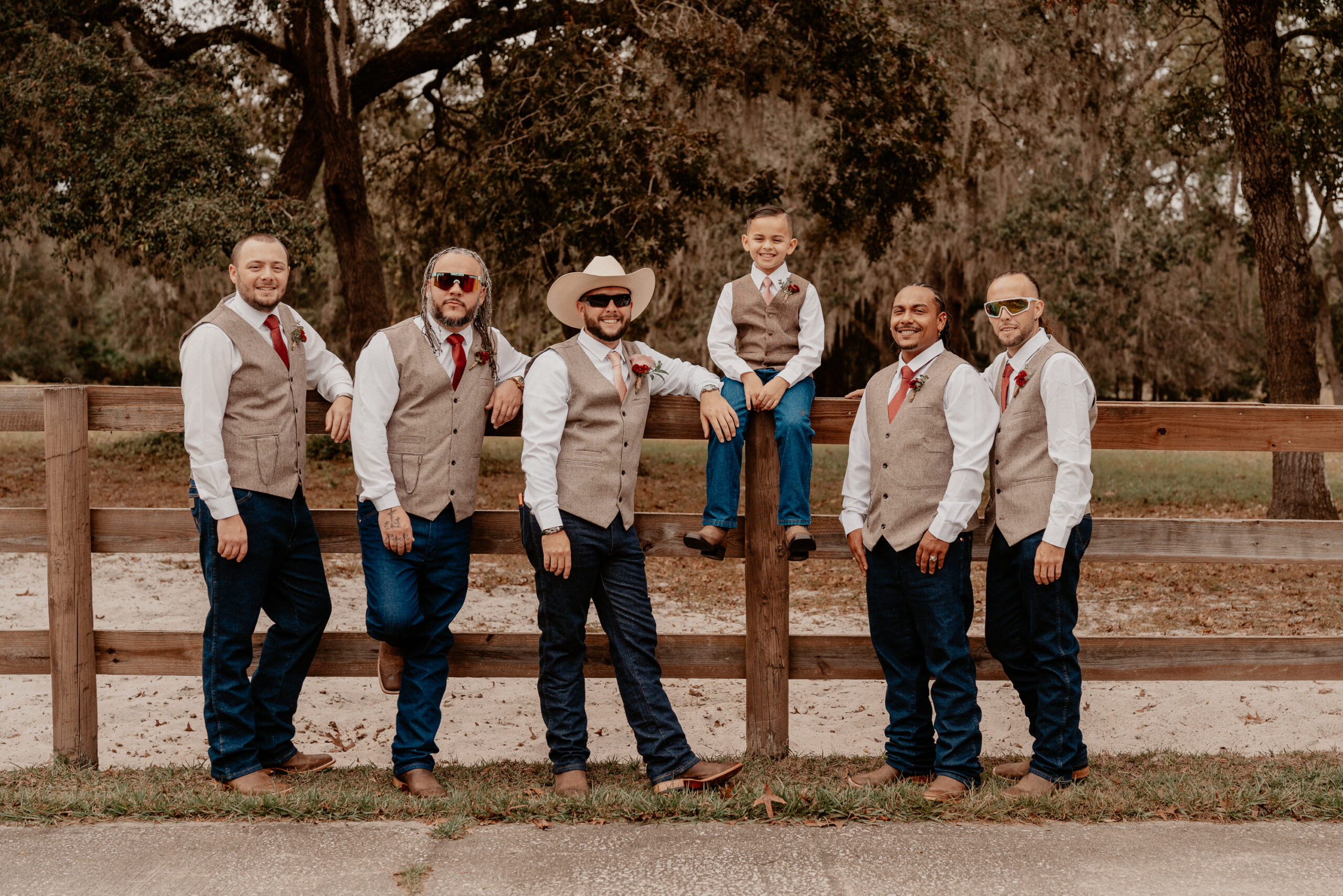 Groomsmen and little boy sitting on a fence in front of a rustic field