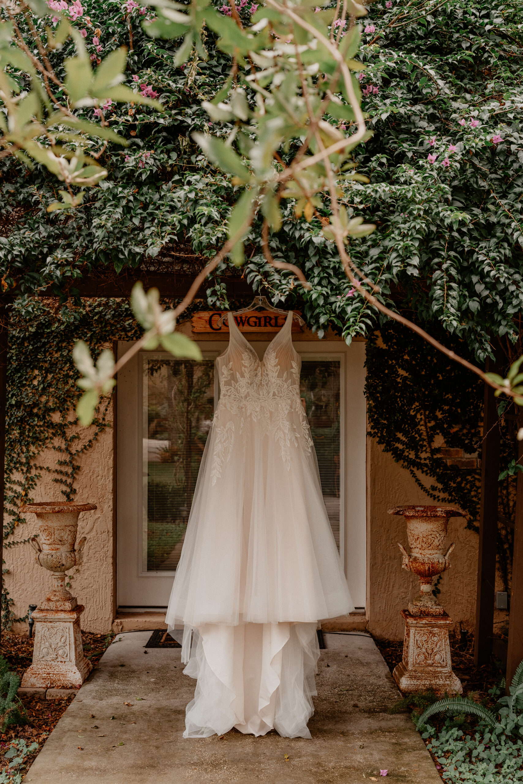 Wedding Dress hanging in front of a rustic door surrounded by greenery