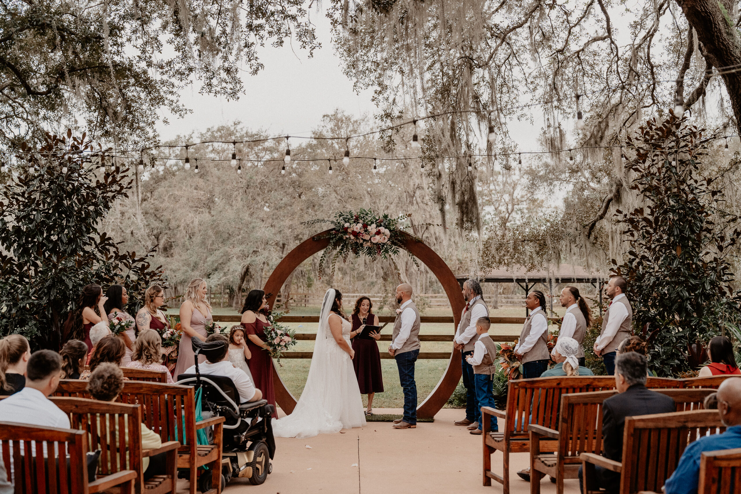 Bride and groom under a wooden circle with flowers exchanging vows